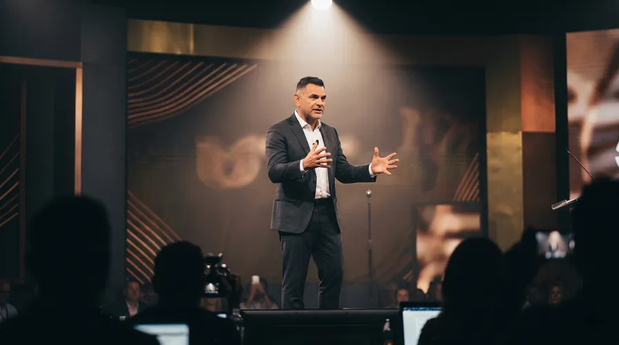 Will Turner speaking on a gold-lit conference stage